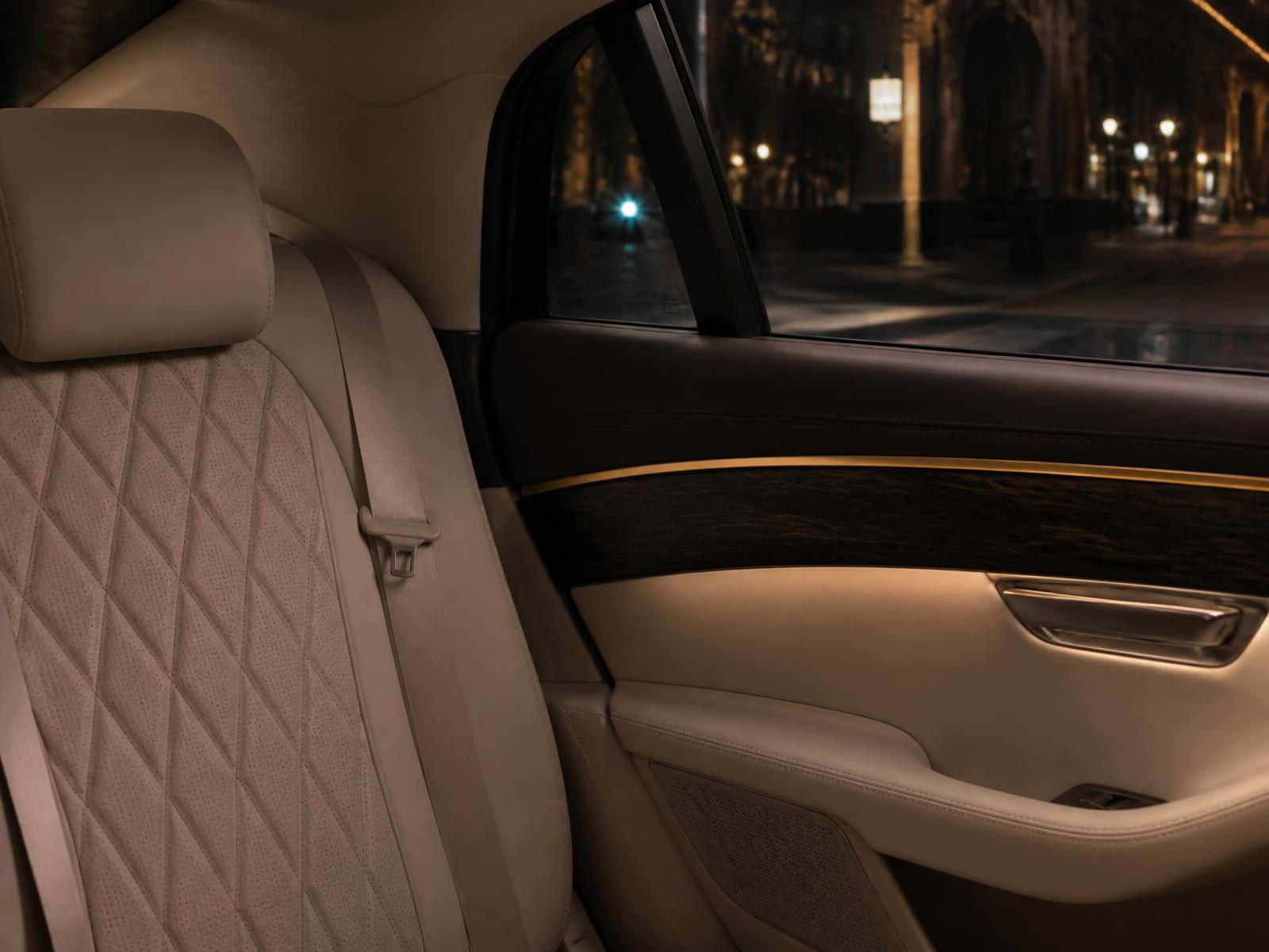 The rear seat of a chauffeur-driven car at night, in cream leather and dark wood